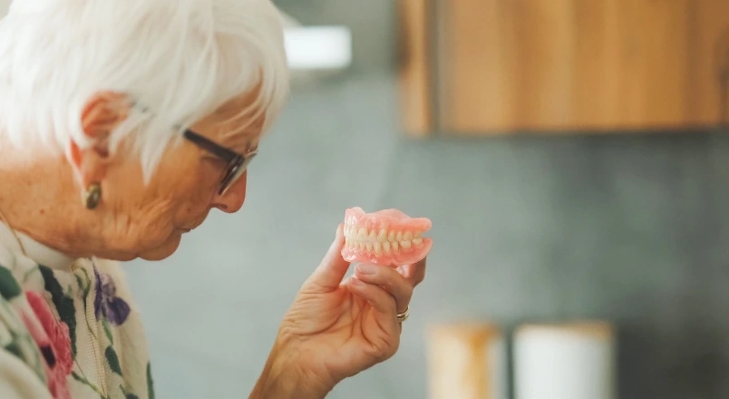 Older patient holding a removable denture while considering tooth-replacement options.