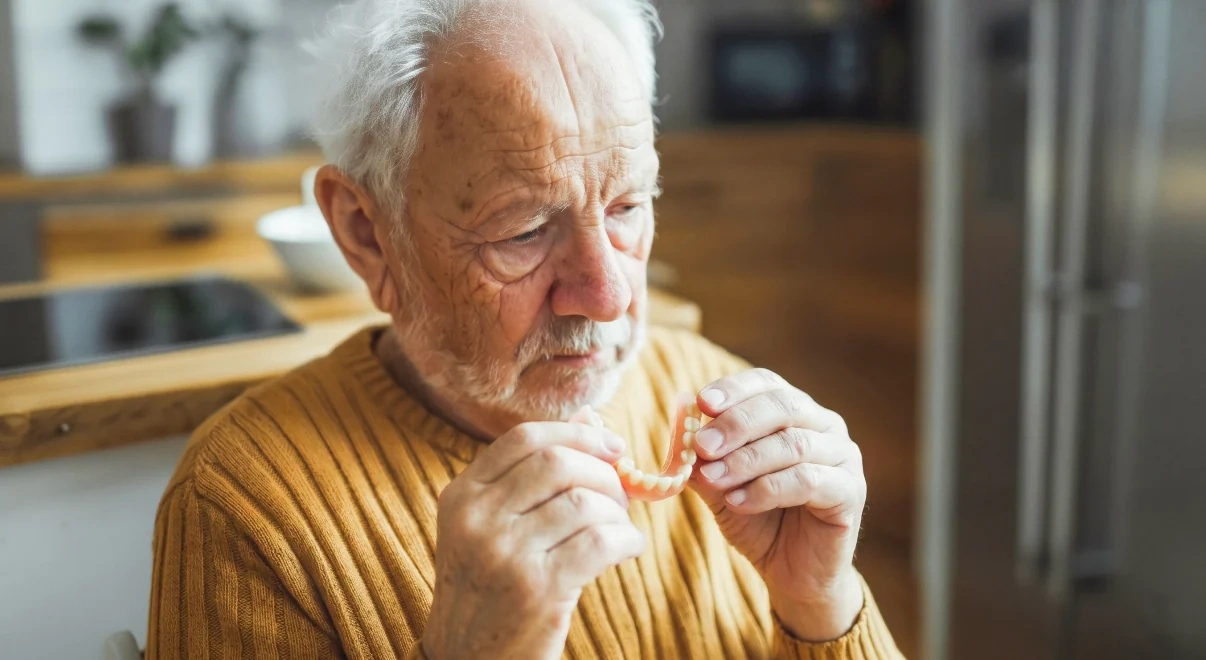 Older patient holding a removable denture while considering full-arch replacement options.