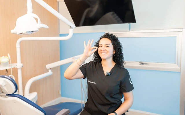 Dentista de hisonrisa sosteniendo una corona dental en un consultorio.