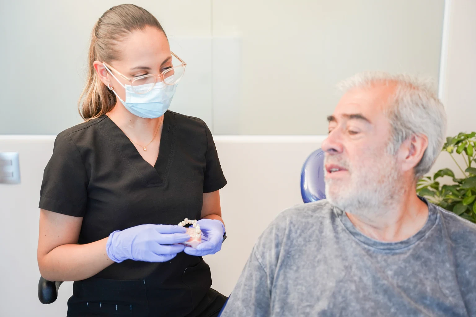 Dentist holding a dental model beside a patient during a crown material planning conversation.